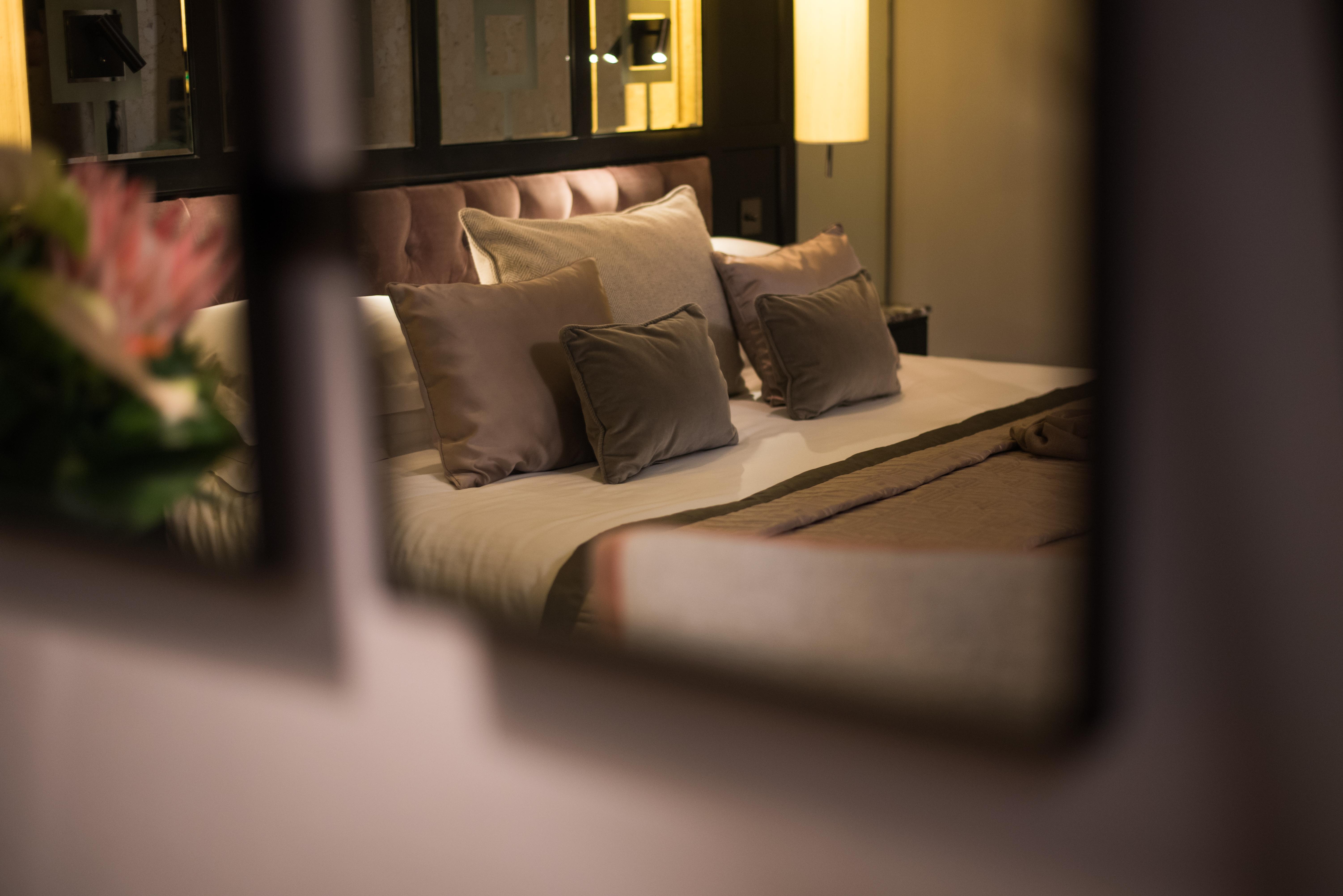 The Fitzwilliam Hotel Belfast Bagian luar foto The photo shows a cozy and elegantly decorated bedroom. The focal point is a plush bed with soft, neutral-colored bedding and several decorative pillows arranged neatly on it. The room has a warm ambiance, enhanced by a standing lamp that provides so
