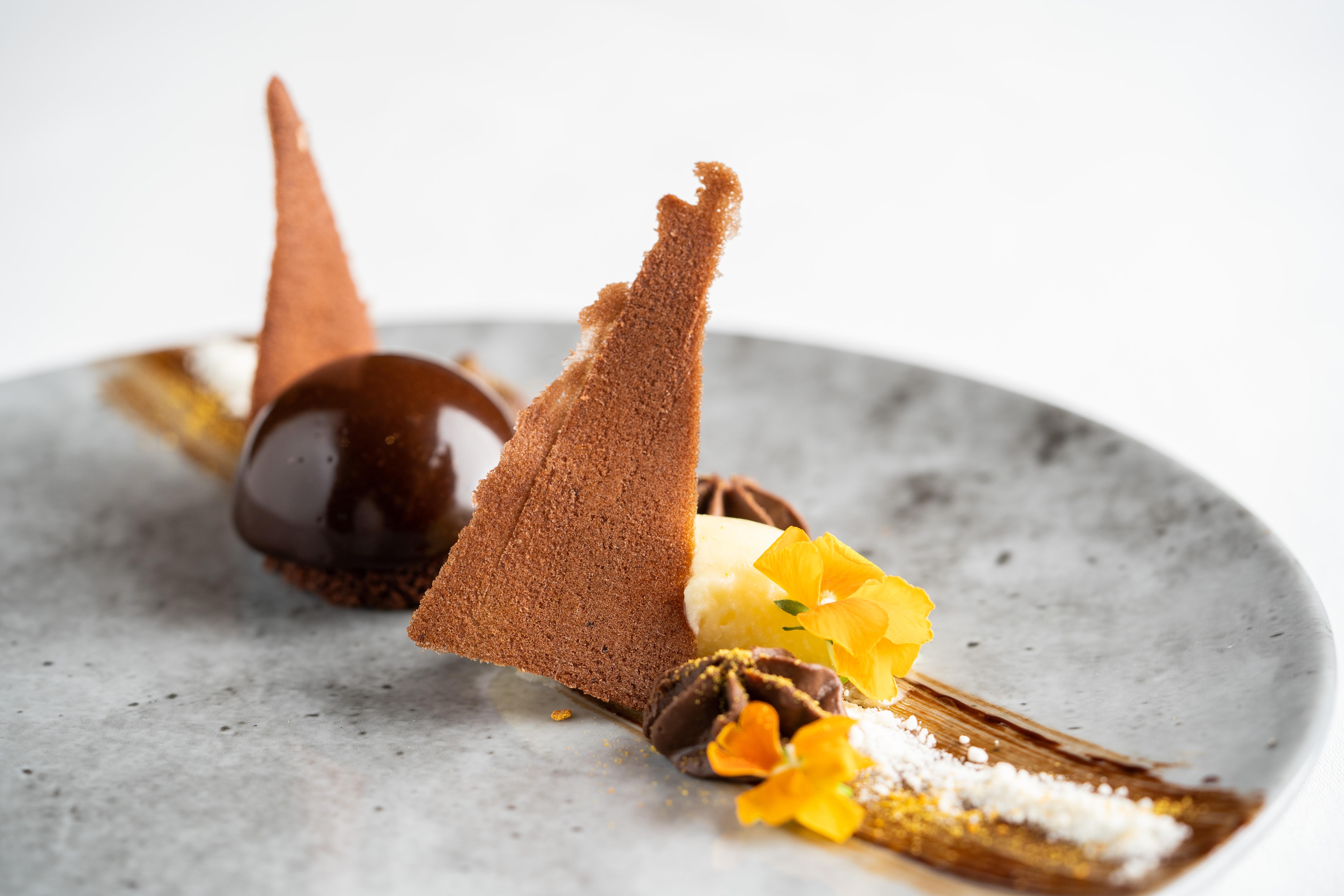 The Fitzwilliam Hotel Belfast Bagian luar foto The photo displays an artfully plated dessert. It features a glossy chocolate sphere, accompanied by various chocolate components, including triangular chocolate tuile pieces that resemble sails. The plate is adorned with delicate garnishes such as y