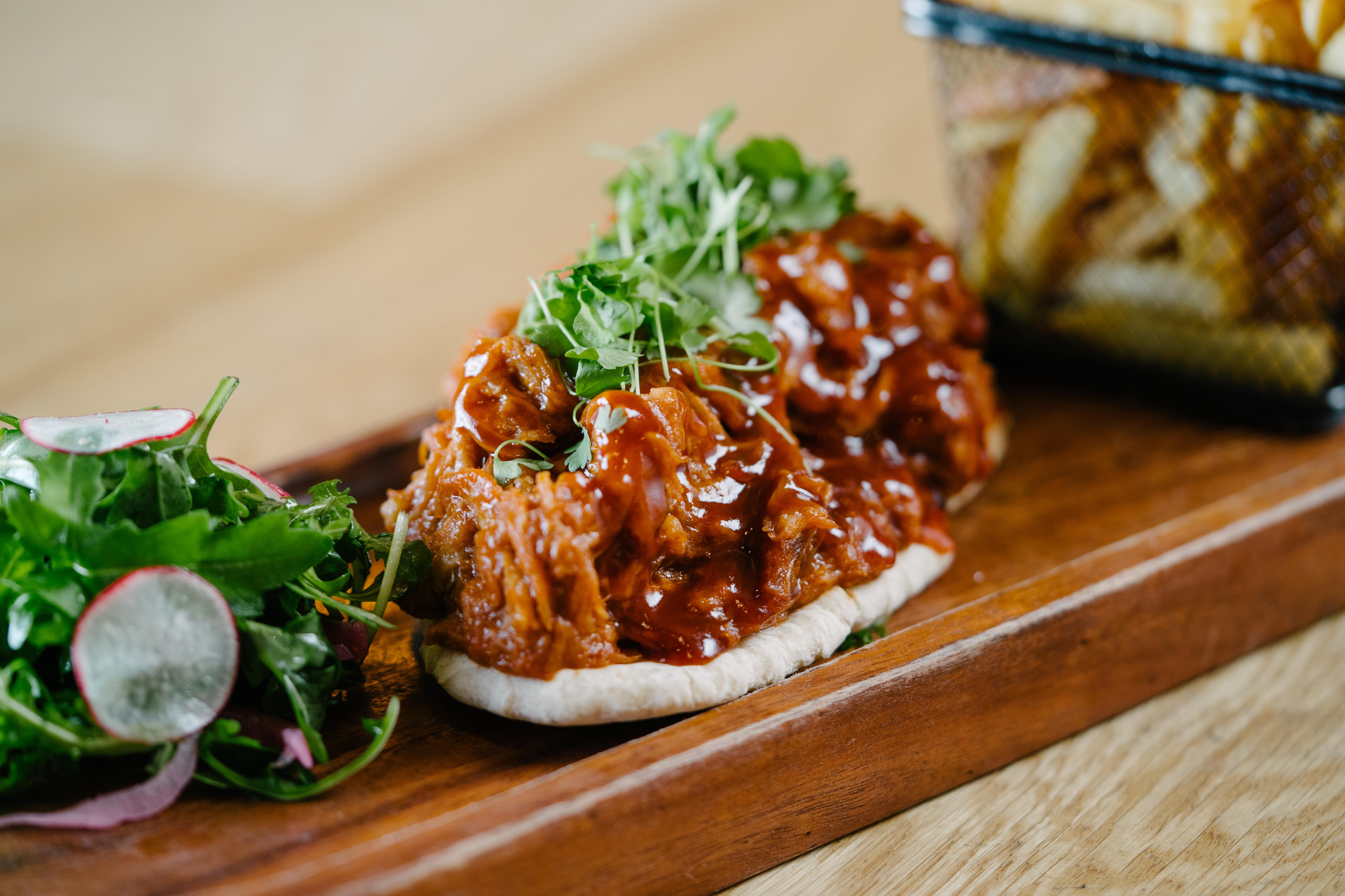 The Fitzwilliam Hotel Belfast Bagian luar foto The photo shows a wooden platter featuring two pieces of bread topped with pulled meat covered in a rich barbecue sauce. The dish is garnished with fresh greens, including sprouts. On the side, there is a small serving of mixed salad with radishes an